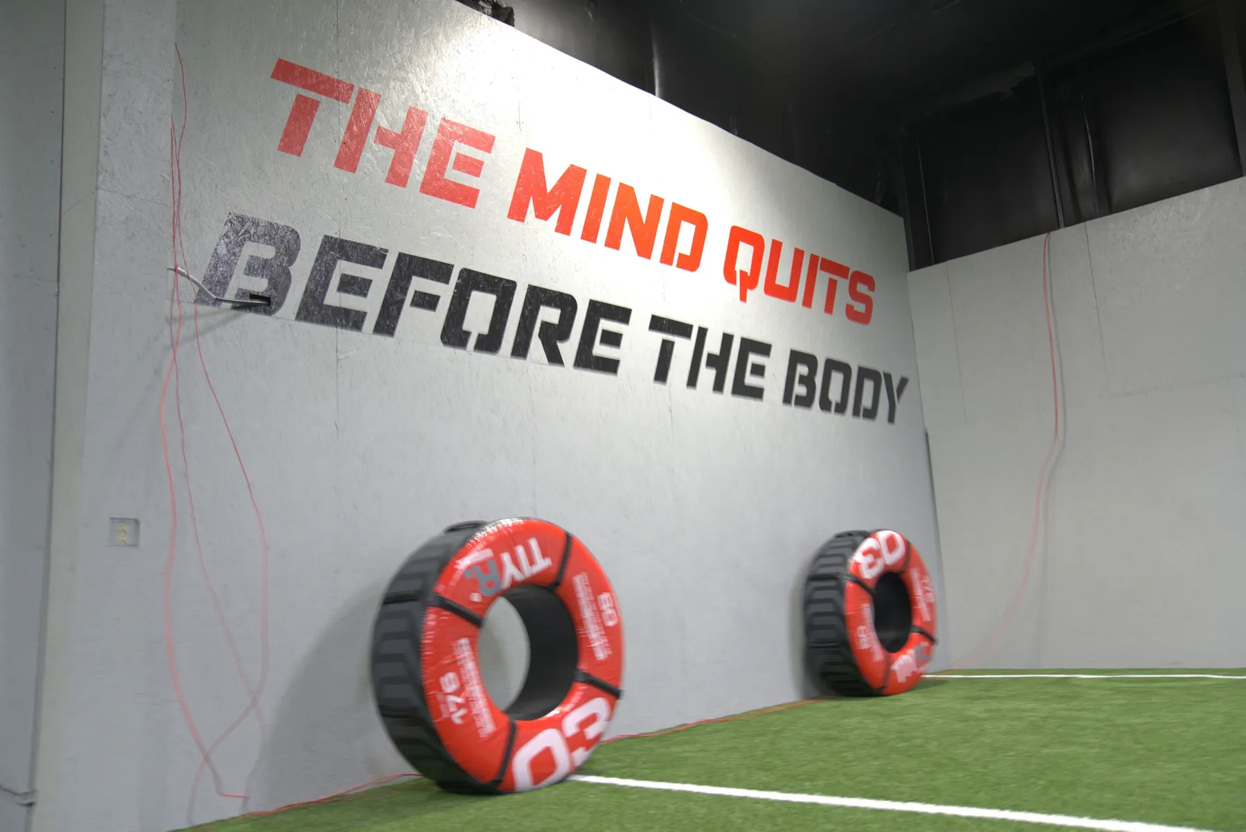 “The mind quits before the body” painted in red and black across the facility wall, with training tires stacked beneath it.